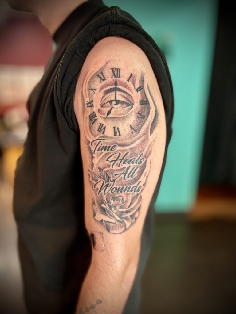 Clock and lettering upper arm tattoo by Sideshow Tattoo and Piercing San Diego