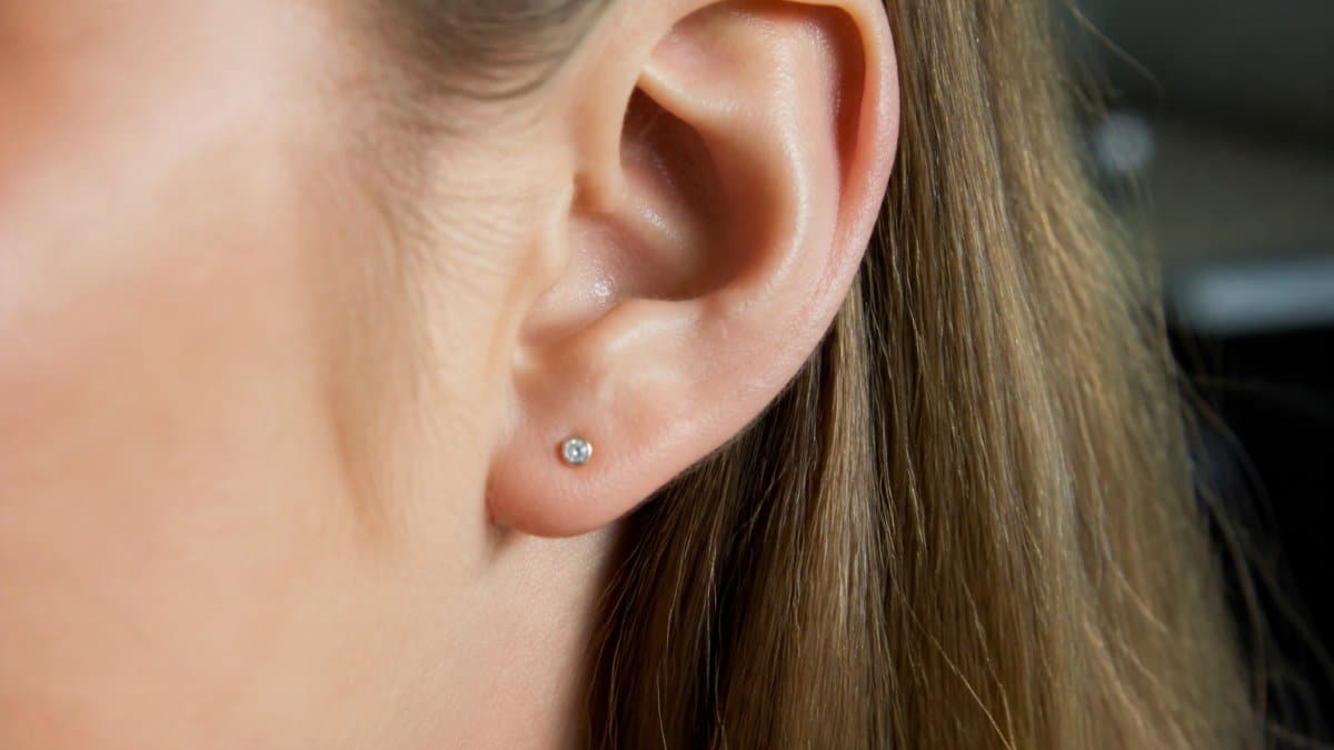 Close-up of a person's earlobe wearing a flat-back stud earring, showing the low-profile design sitting flush against the skin with clear detail of the secure backing
